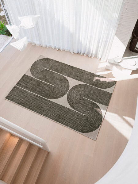 A rectangular area rug with a modern abstract design of two large winding dark gray loops on a light beige background, styled on a light wood staircase landing.