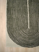 A close-up of a textured area rug with a bold black concentric arch pattern on a light beige background, shown on a light wood floor.