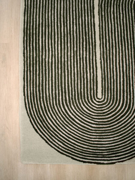 A close-up of a textured area rug with a bold black concentric arch pattern on a light beige background, shown on a light wood floor.