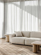 Beige sofa in a modern living room with light curtains and wooden coffee tables.