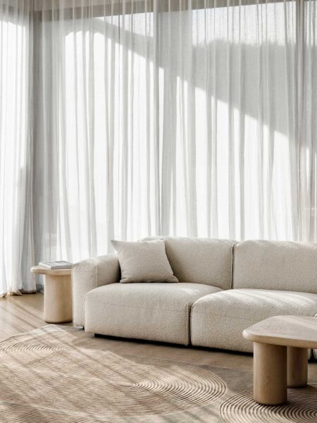 Beige sofa in a modern living room with light curtains and wooden coffee tables.