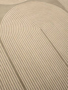 A close-up of a textured area rug featuring a modern, minimalist concentric arch pattern in warm beige and cream tones.