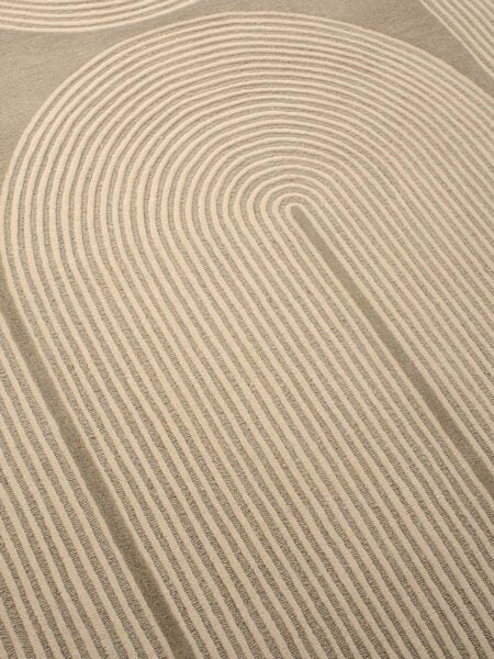 A close-up of a textured area rug featuring a modern, minimalist concentric arch pattern in warm beige and cream tones.