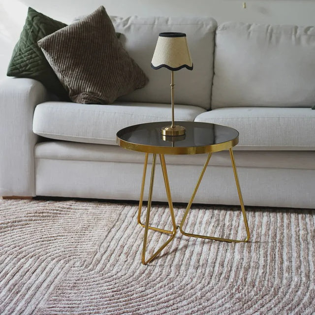 Gold side table with a lamp on a beige sofa with decorative pillows.