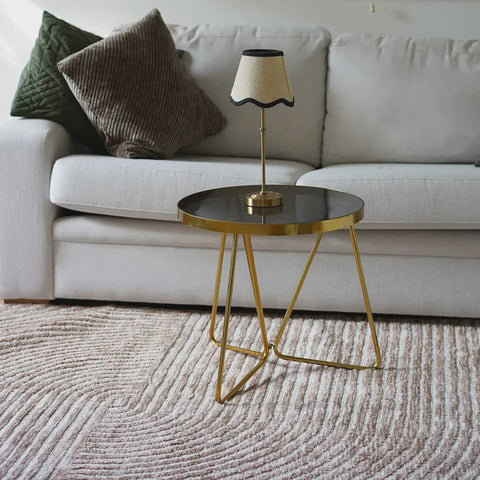 Gold side table with a lamp on a beige sofa with decorative pillows.