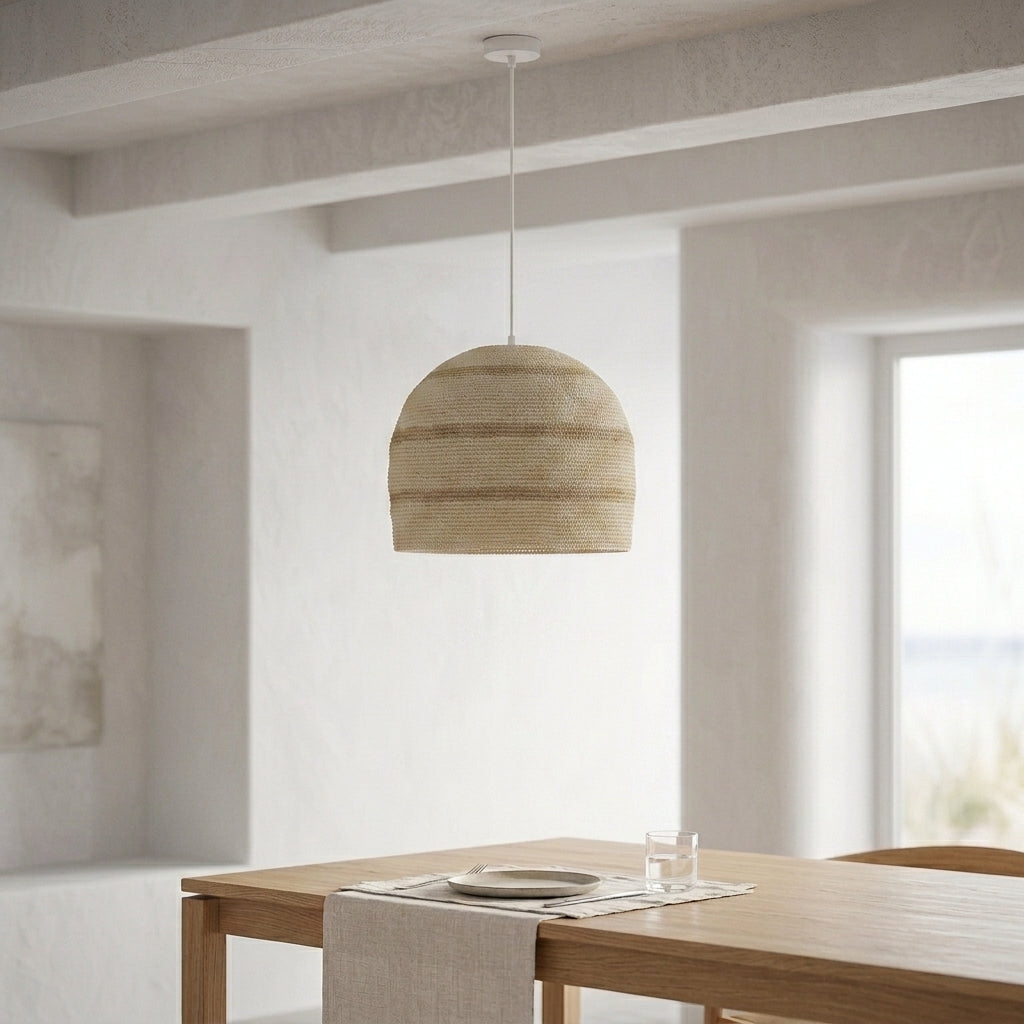 A woven dome-shaped pendant light in a natural beige tone hangs over a wooden dining table in a bright, modern room with textured white walls and a window.