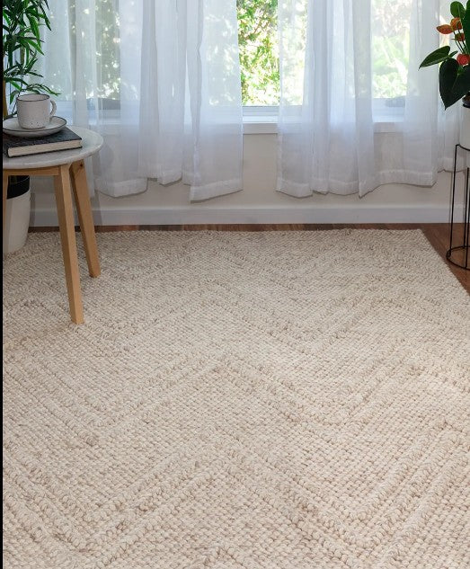Beige woven rug in a room with white curtains and plants.