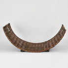 A curved, hand-woven basket or tray with integrated handles and small feet, shown against a plain light gray studio background.