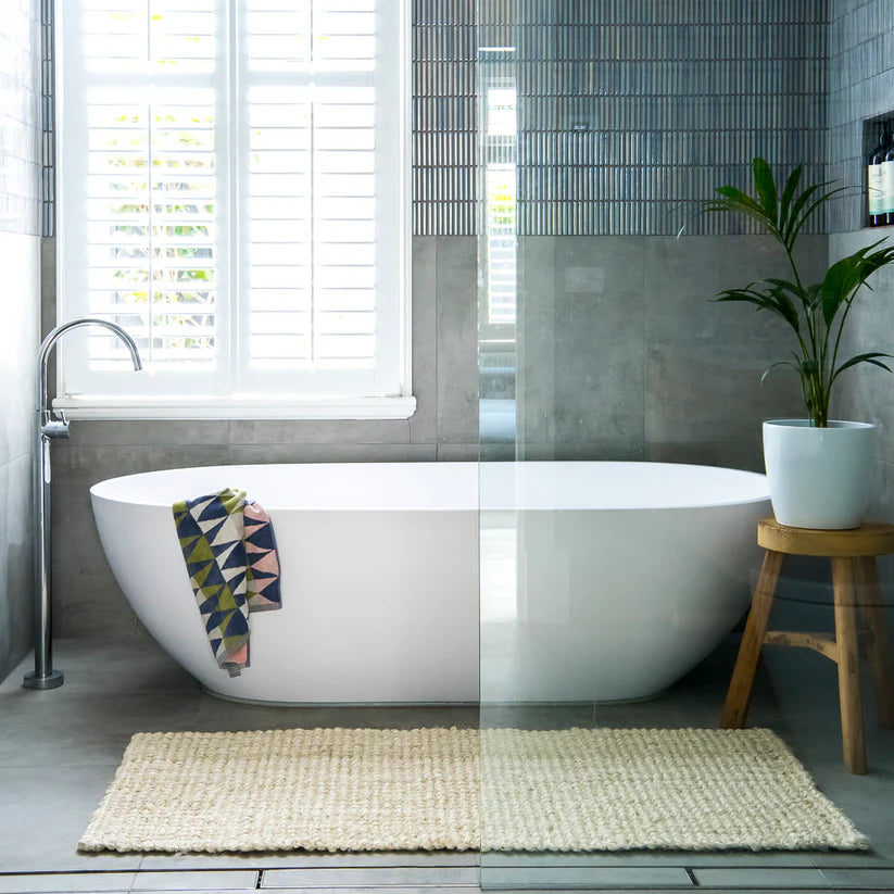 Modern bathroom with a freestanding bathtub, plant, and rug.