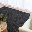 Dark gray rug on a wooden floor with a plant and chair in the foreground