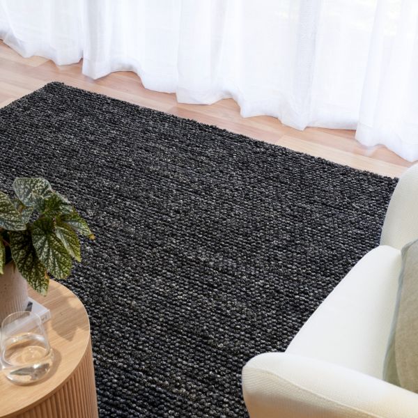 Dark gray rug on a wooden floor with a plant and chair in the foreground