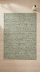 Green rug on a wooden floor with a white vase on the right side.