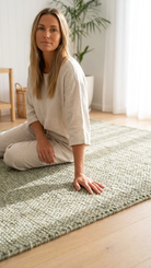 Woman sitting on a green rug in a room with white walls and a plant.