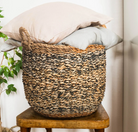 Woven basket with pillows on a wooden stool against a neutral wall.
