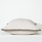 A square throw pillow in a light beige fabric with a contrasting textured gray braided trim along the edges, shown against a plain white background.