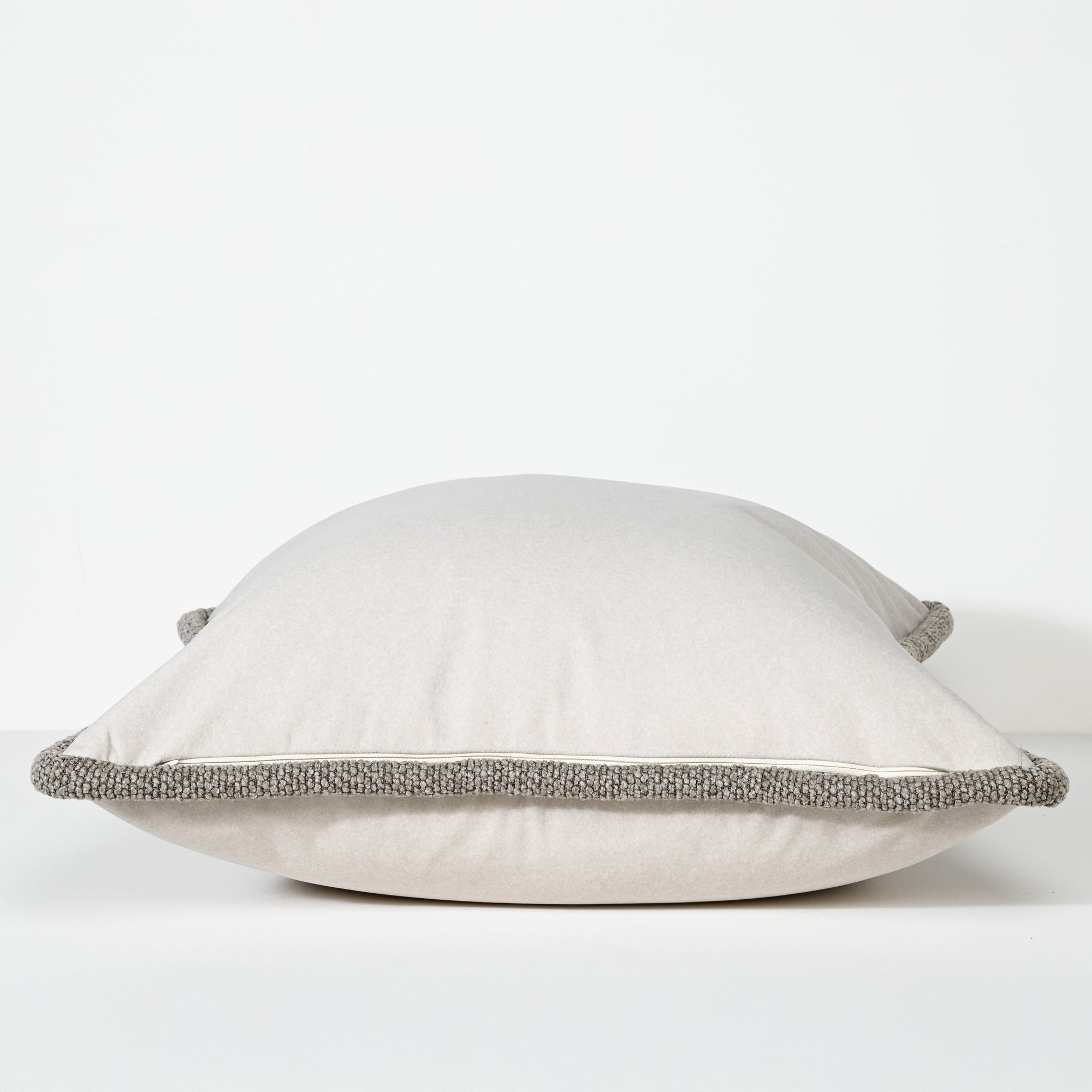 A square throw pillow in a light beige fabric with a contrasting textured gray braided trim along the edges, shown against a plain white background.