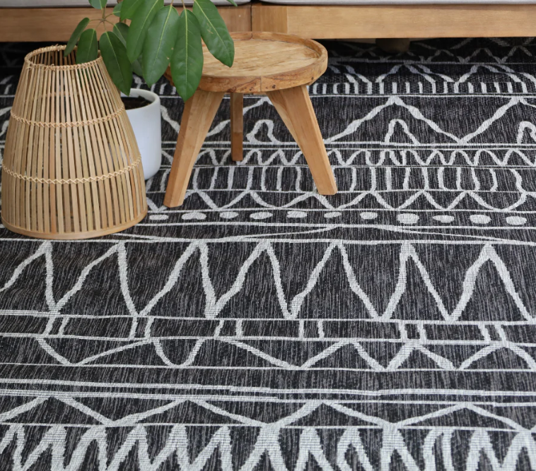 Patterned rug with a wooden stool and plant in the background