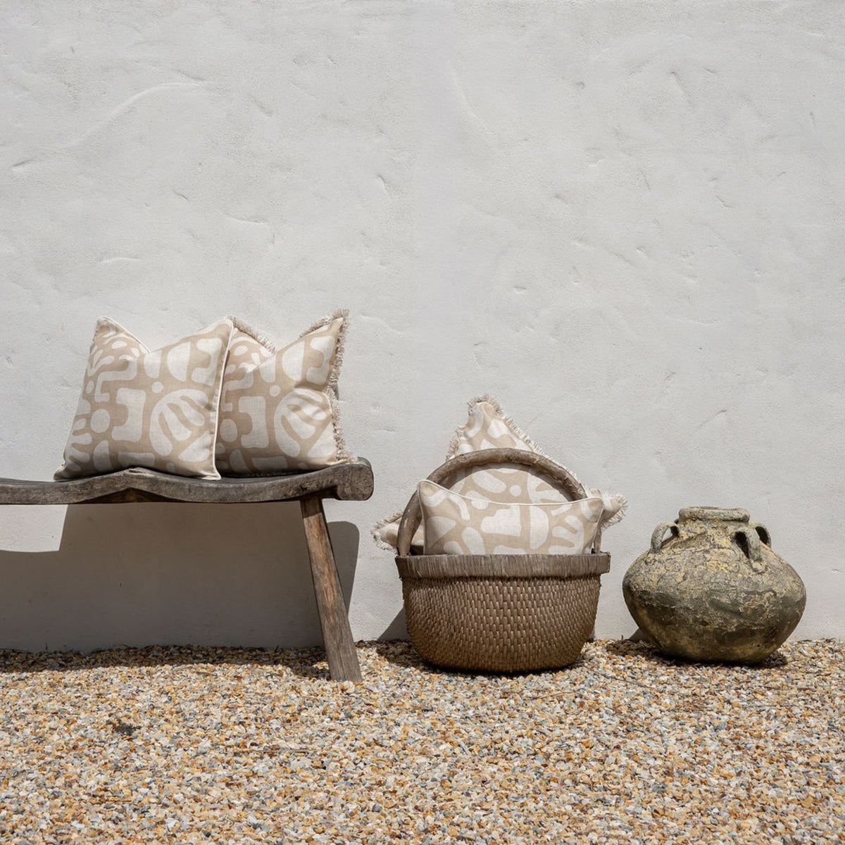 Decorative pillows on a wooden bench and woven basket against a textured wall.