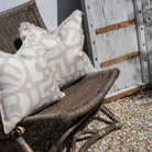 Wicker chair with patterned cushions against a rustic wooden wall.