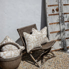 Wicker chair with patterned cushions against a rustic wooden door.