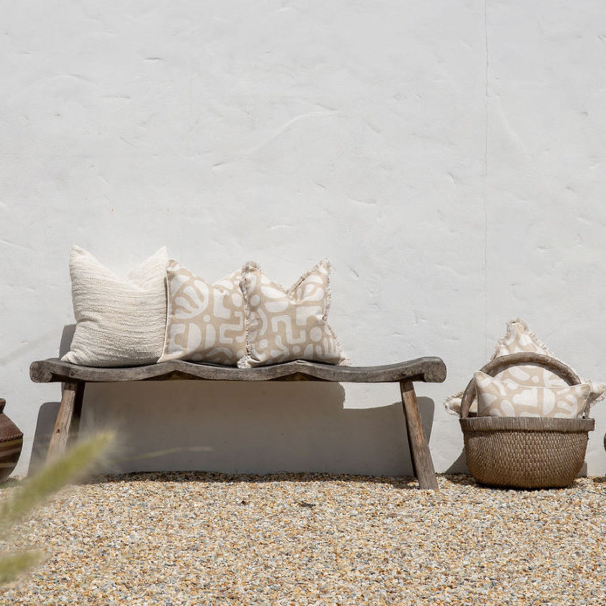 Wooden bench with decorative pillows against a light gray wall.