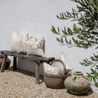 Decorative pillows on a wooden bench with rustic pots and a plant in the background