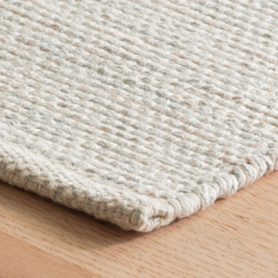 Close-up of a textured beige rug on a wooden floor