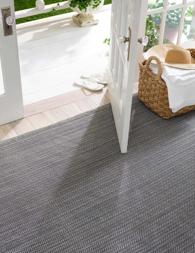 Gray patterned outdoor rug on a patio with a white door and basket in the background.