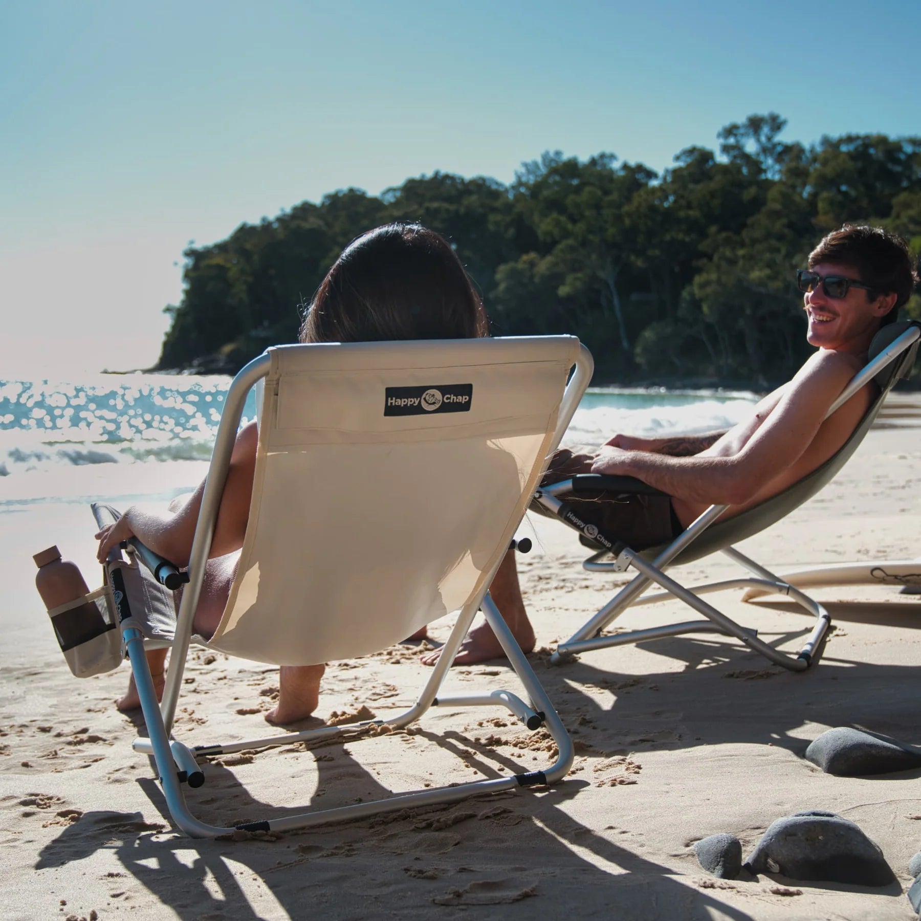Two people sitting on beach chairs at the beach with a clear sky.