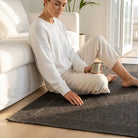 Woman sitting on a dark rug holding a mug in a bright living room.