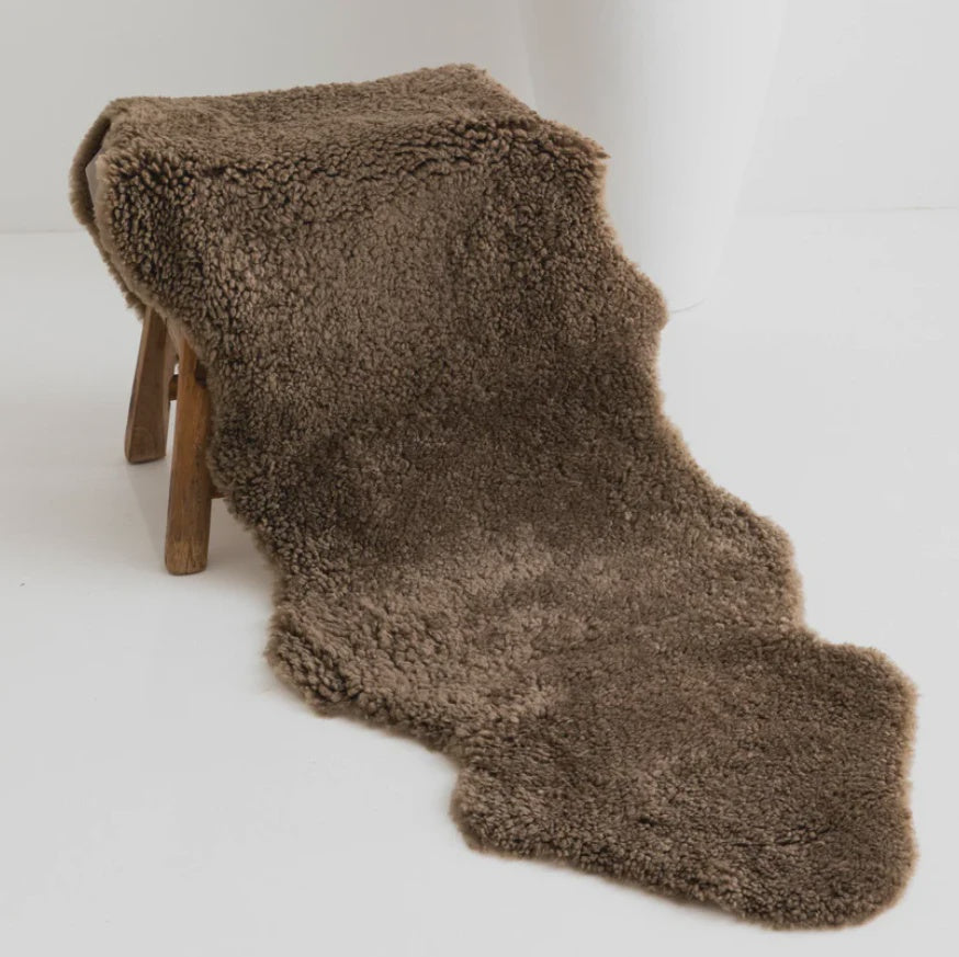 Brown sheepskin rug draped over a wooden stool on a white background