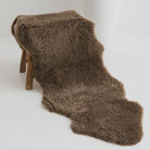 Brown sheepskin rug draped over a wooden stool on a white background