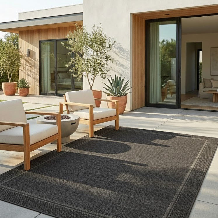 Modern outdoor patio with a black rug, wooden chairs, and potted plants.