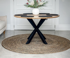 Round wooden table with black metal legs on a woven rug in a room.