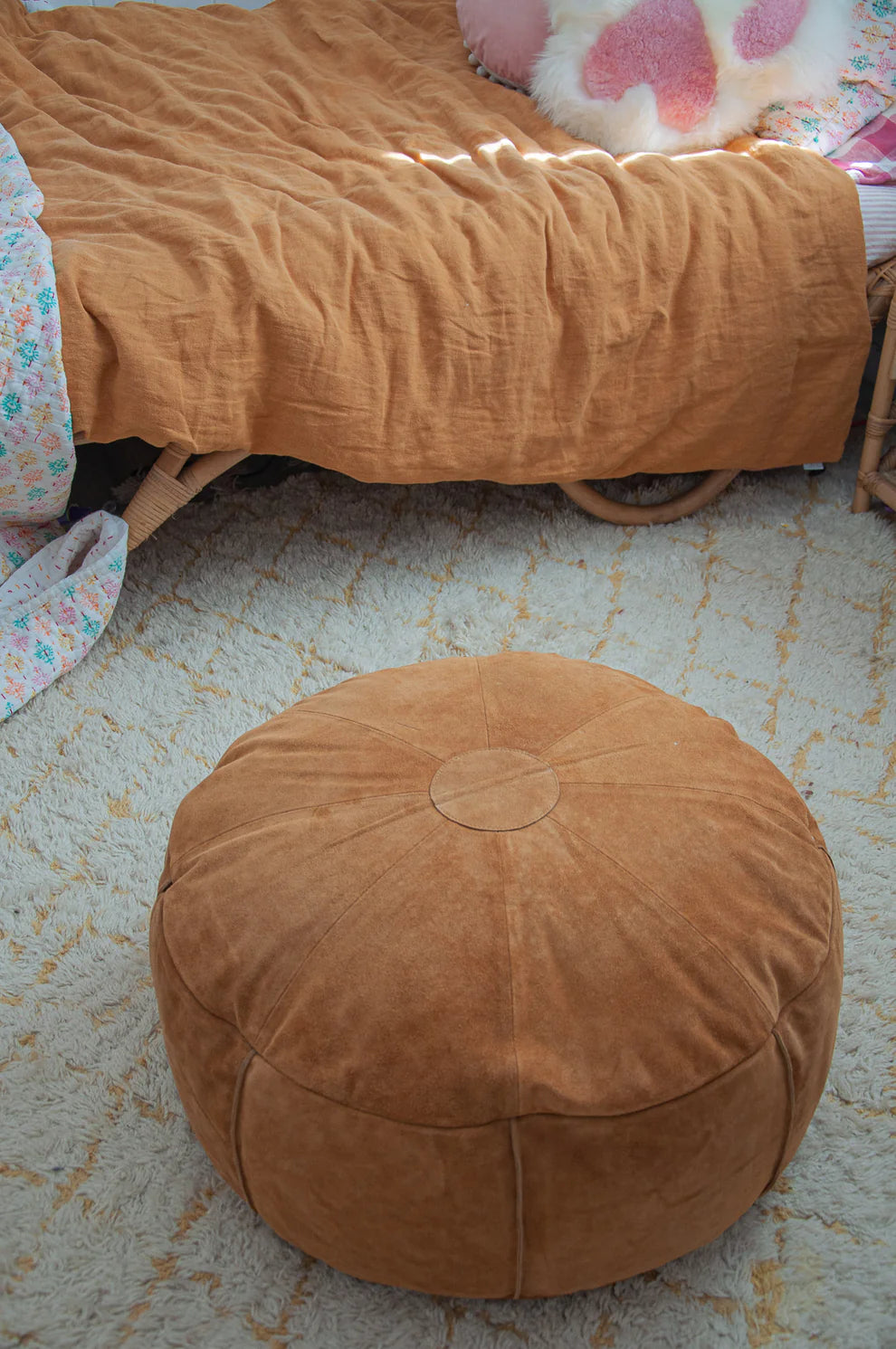 Brown ottoman on a textured floor with a bed and blanket in the background