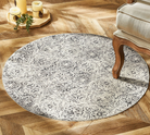 Round patterned rug on a wooden floor with a chair and candle holder in the background.