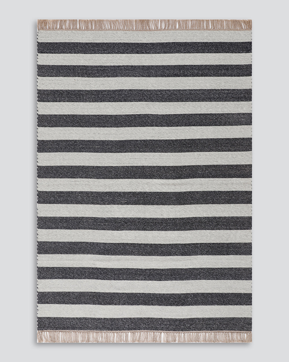 A rectangular woven rug with horizontal stripes in dark charcoal gray and off-white, finished with fringed edges on all sides, shown flat against a light gray background.