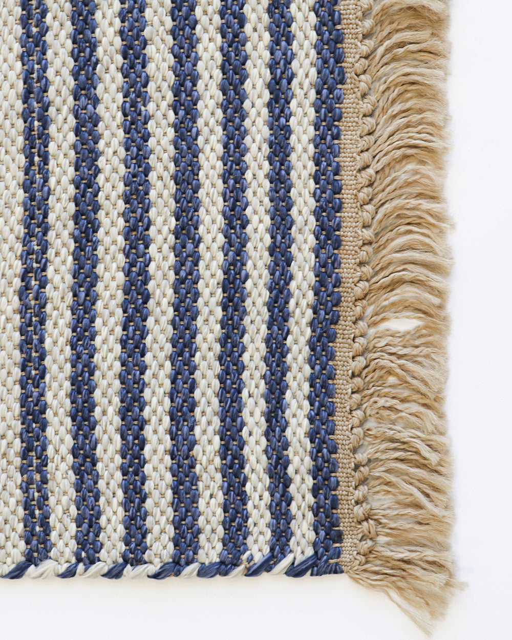 Close-up of a woven textile with vertical navy and cream stripes and a beige fringe along the right edge, shown on a white background.