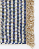 Close-up of a woven textile with vertical navy and cream stripes and a beige fringe along the right edge, shown on a white background.
