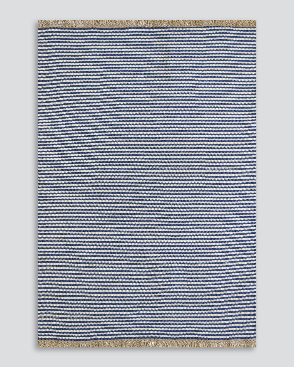 A rectangular woven rug with narrow horizontal navy and off-white stripes, finished with natural beige fringe on the top and bottom edges, shown against a neutral light gray background.