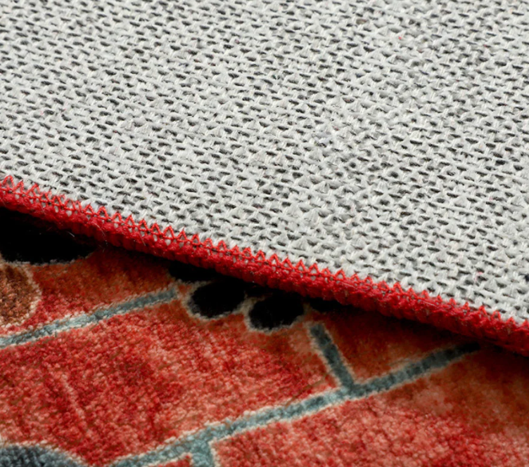 Close-up of a textured gray rug with a red border on a brick-patterned floor.