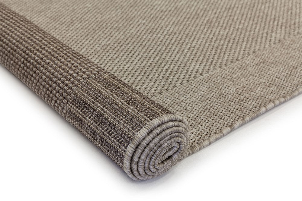 The Noosa Rug's Outdoor Rug in Washed color rolled up, showing both the top and underside, illustrating its versatility and robust construction for various settings.